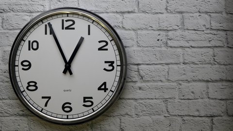 The Time On The Clock One.  A Clock On A White Brick Wall With The Black Arrow Running In The Background Of The Arabic Numerals. Timelapse..