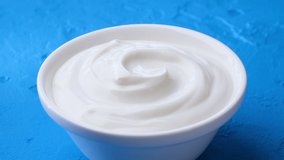 Bowl of sour cream on blue background, greek yogurt with spoon, 4K UHD video footage
