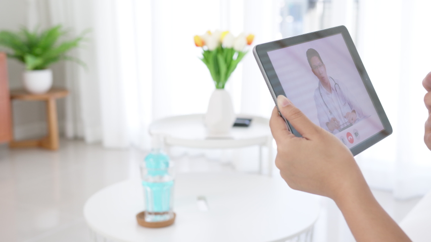Telemedicine concept close up of asian woman video call with doctor at living room home. Patient girl consulting with general practitioner application computer tablet. Doctor and Consultant online | Shutterstock HD Video #1056135377