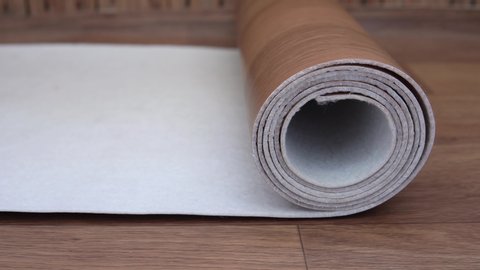 Roll of brown linoleum unfolds on the floor. No people. Close-up video. Brown linoleum with wood structure. Construction work at home. 4K resolution