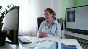 health care, female doctor consults an online patient telling symptoms of disease using an x-ray using a video link on computer and webcam sitting in medical office
