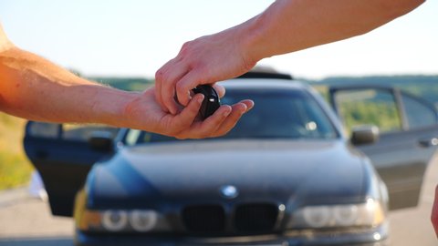 Unrecognizable man getting car key from seller. Male hands giving keys of car to his friend outdoor. Handshake between salesman and new owner of automobile after deal. Slow motion Close up