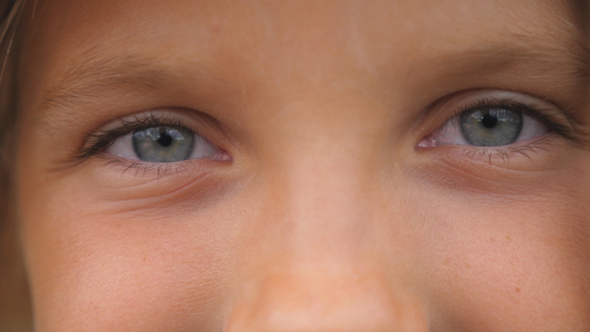 Close up of blue eyes of happy small girl blinking and looking into camera with a happy sight. Portrait of cute face of young smiling child watching with positive emotion. Front view | Shutterstock HD Video #1056139355