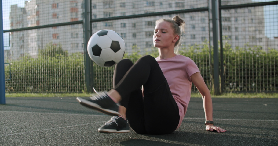Young caucasian girl practicing soccer skills and tricks with the football ball at sunset in an playground. Urban city lifestyle outdoors concept. 4K UHD slow motion RAW graded footage