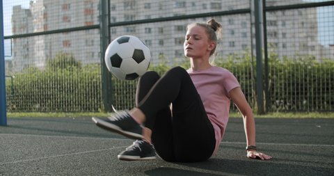 Young caucasian girl practicing soccer skills and tricks with the football ball at sunset in an playground. Urban city lifestyle outdoors concept. 4K UHD slow motion RAW graded footage Video stock
