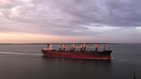 Tracking aerial of cargo bulker on its tranportation voyage during sunset. Merchant vessel with dry freight loaded with grain or coal heading to seaport. Ship deliver wheat or corn. Maritime industry