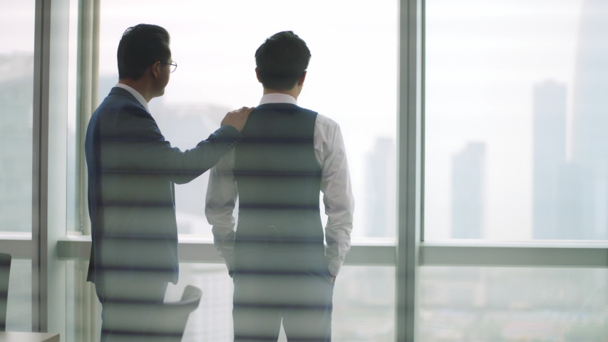 Mature asian manager comforting young business man standing in front of window | Shutterstock HD Video #1056144299