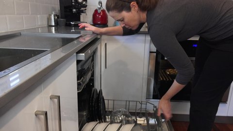 Adult woman (female age 30-40) loading dishes into a dishwasher at home kitchen.Real people. Copy space