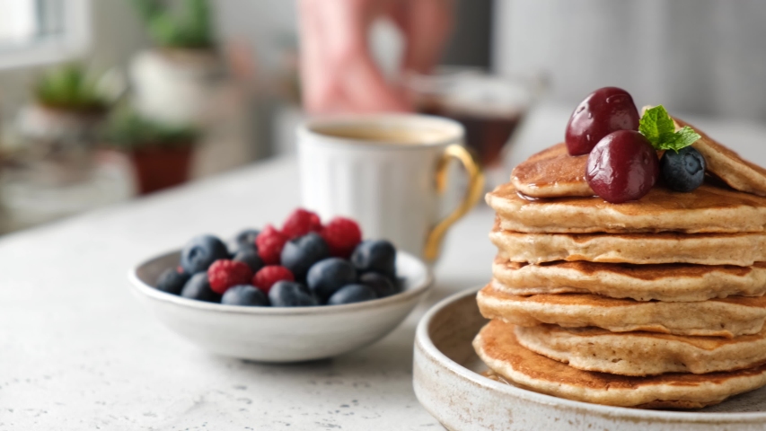 Pouring maple syrup on stack of pancakes. Delicious whole wheat oat pancakes with berries and maple syrup, stack of vegan pancakes for breakfast Royalty-Free Stock Footage #1056145439