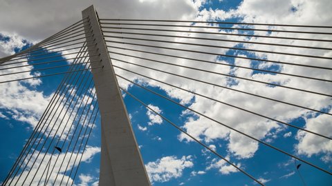 Pylon of a cable stayed bridge under fast moving white and gray clouds in blue sky. Time lapse footage. Millennium bridge in Podgorica Montenegro.