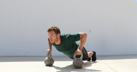 Fitness man strength training body core doing push-ups holding on kettlebells bodyweight floor exercises at outdoor gym.