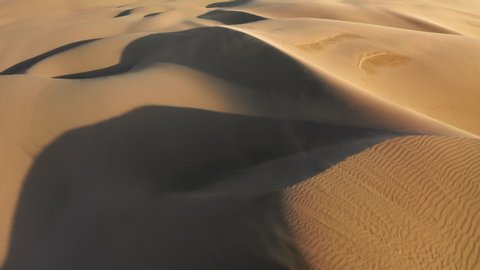 Incredible aerial shot of strong wind blowing away the golden sand from the tops of high dunes in sunset light. Cinematic background with ripples texture on the surface of desert nature