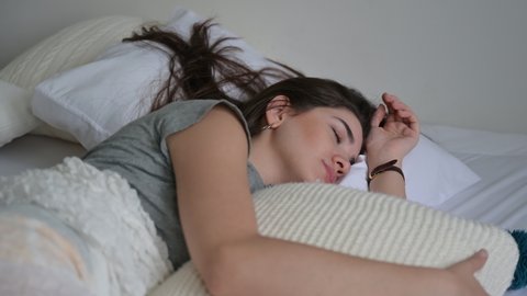 Calm young woman sleeping well in comfortable cozy white bed with soft pillow, peaceful serene girl resting lying asleep enjoying healthy good sleep nap in the morning at home