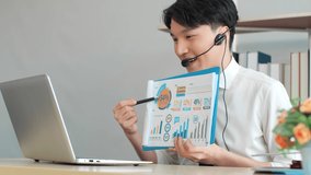 Asian businessman wear wireless headset communicating by explain stock graph documents looking at computer laptop in office, video chat job interview.
