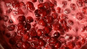 Homemade cooking. Video clip of active making cherry jam boiling process. Preparation of sweet cherry confiture and mixing it with wooden spoon. Top view, top down food. Close-up.
