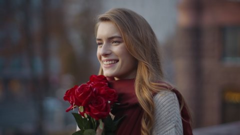 Portrait of cute hipster girl smelling bouquet of flowers outdoors. Closeup sweet woman holding floral bunch in hands outside. Smiling female person carrying roses on city street.