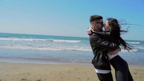 Lifestyle close up portrait of young stylish couple guy and girl hugging neck guy twisting in arms and kissing on nature background, sea landscape. Happy man and woman. Love story beach