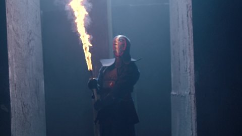 Portrait of a Japanese kendo fighter hold a burning sword . Epic Kendo warrior stands in armor in the fog and looking at the camera with his fire shinai . Mysterious video scene . Shot on Arri Alexa .