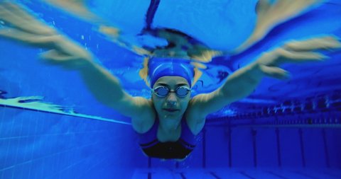 Under water view of professional female swimmer . Underwater footage of woman jumping into water . Swimmer jumping in big swimming large pool. Woman swimmer dive in water pool .  Slow Motion .