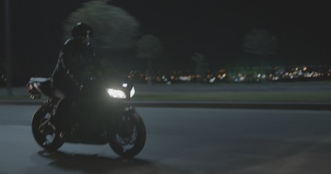 Biker with super sport motorcycle .  All in black Motorcyclist riding fast on city road at night . Motorcycle adventure lifestyle . Fast riding of black biker . Shot on ARRI ALEXA Cinema Camera .