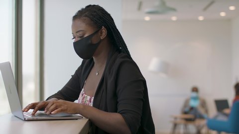 Back at work with social distance precautions. A black woman at a tech firm works on her laptop. Business is back. Shot in slow-motion and in 4k. 