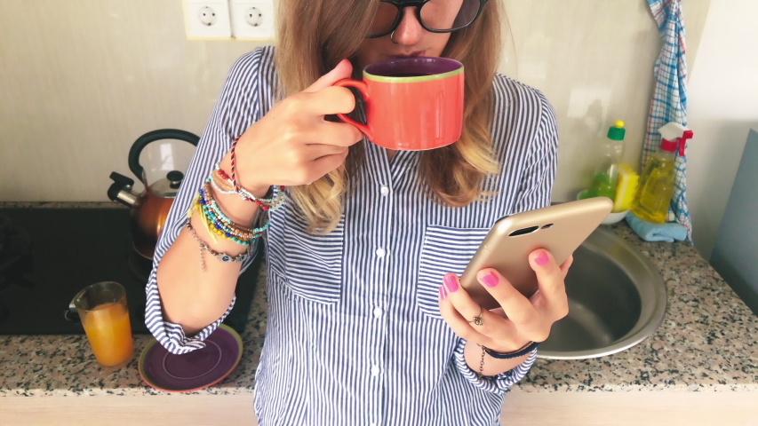 Cute girl drinking fresh orange juice and using cellphone in the kitchen.	
