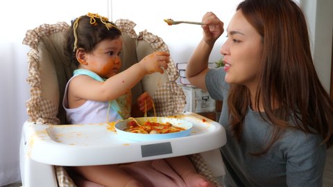 Asian babysitter like to tease little girl by do not feeding food to poor toddler baby girl and kid want to eat by grab spoon from nursemaid. Adorable toddler baby get unhappy, upset, unsatisfied her