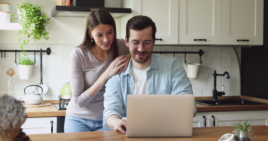 Spouses spend time on rented home kitchen look at pc screen laughing receive e-mail from bank feels excited, loan accept, on-line betting win, lottery victory. Moment of sincere happy emotions concept Royalty-Free Stock Footage #1056179009