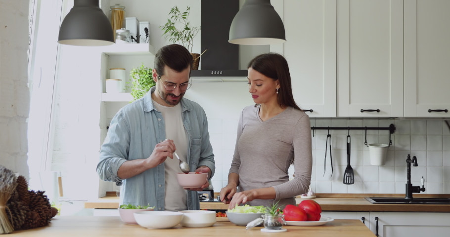 Loving couple feed each other while cooking together in modern kitchen enjoy conversation and healthy vegetarian salad food preparation. Lifestyle, happy homeowners, romantic date, hobby, love concept | Shutterstock HD Video #1056179024