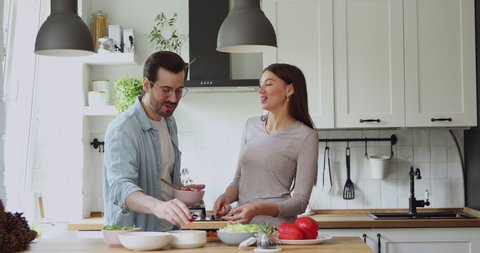 Loving couple feed each other while cooking together in modern kitchen enjoy conversation and healthy vegetarian salad food preparation. Lifestyle, happy homeowners, romantic date, hobby, love concept
