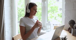 20s woman sit at desk in front of laptop look at pc screen lively chatting with friend, listen tutor, interact through wireless headphones. Distant talk, job interview, study, video call event concept
