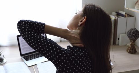 Tired young woman sit at desk massaging neck rubbing tensed muscles after long usage of laptop rear back close up view. Incorrect poor posture, sedentary lifestyle, need exercises or treatment concept