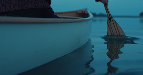 CU view of a paddle, man canoeing alone boat on a large lake at dawn. Shot on RED cinema camera with 2x anamorphic lens