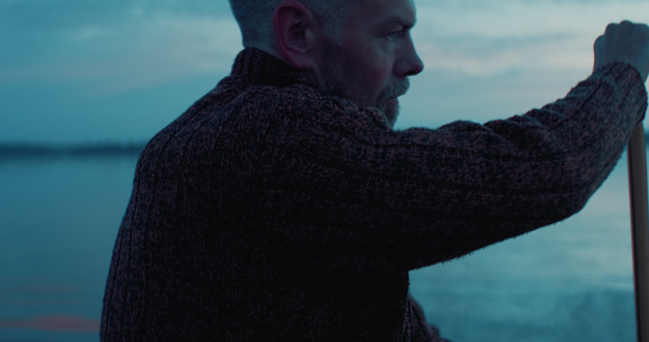Portrait of mid 50s man canoeing alone boat on a large lake at dawn. Shot on RED cinema camera with 2x anamorphic lens