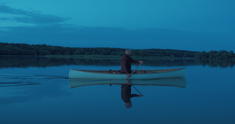 Man canoeing in a traditional wooden boat on a large lake at dawn. Shot on RED cinema camera with 2x anamorphic lens