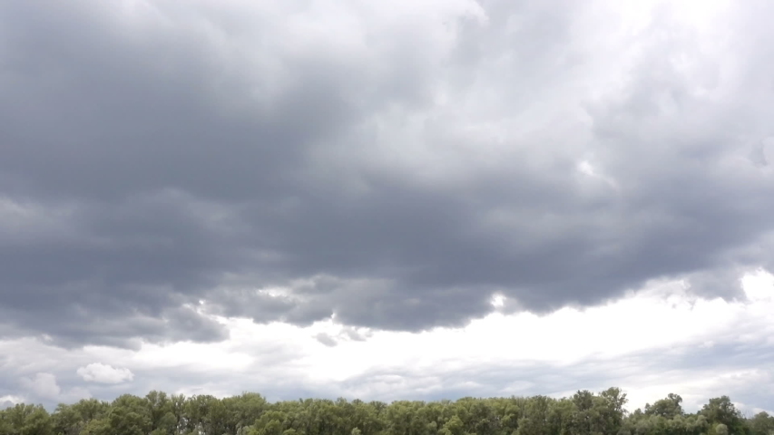 Time lapse gray rain clouds float in the sky above the forest.