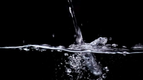 Water drops are pouring into the water surface in slow motion on a black background. Abstract splashes, bubbles and waves of water on black