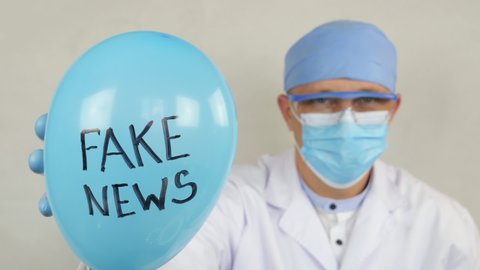 Fake News words on the blue balloon. Physician holds a balloon with the inscription Fake News. The doctor punches a balloon with a medical needle.