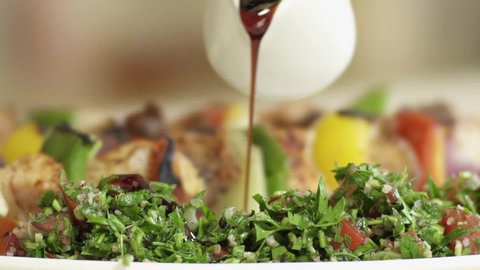 Pouring pomegranate molasses on Tabbouleh Salad. Mediterranean cuisine. Roasted meat skewers in the background