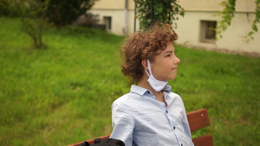 Kid with backpack left school and took off his mask. Schoolboy wearing face mask during epidemic. Back to school concept. Cute boy outside at school having good time