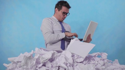 perplexed man office worker with a laptop in a large heaps of crumpled paper