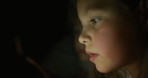 Close up shot of little girl while using a tablet or smartphone in the dark. Concept: future of web technology, video technology, connections and vision of the future of children with the web.
