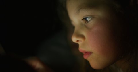 Close up shot of little girl while using a tablet or smartphone in the dark. Concept: future of web technology, video technology, connections and vision of the future of children with the web.