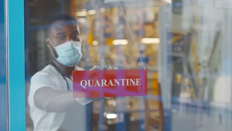 African cafe owner wearing medical mask put quarantine sign on glass door. Afro-american young entrepreneur closing restaurant because of covid-19 pandemic. Small business crisis concept