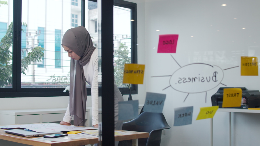 Asia muslim lady drawing work plan think information reminder on paper in new normal office. Working from home, remotely work, self isolation, social distancing, quarantine for coronavirus prevention. Royalty-Free Stock Footage #1056195980