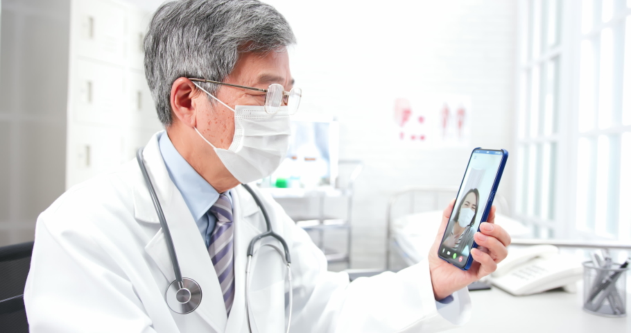 Telemedicine concept - asian senior male doctor explain to the patient about the disease by video chat on cell phone with face mask in clinic | Shutterstock HD Video #1056196730