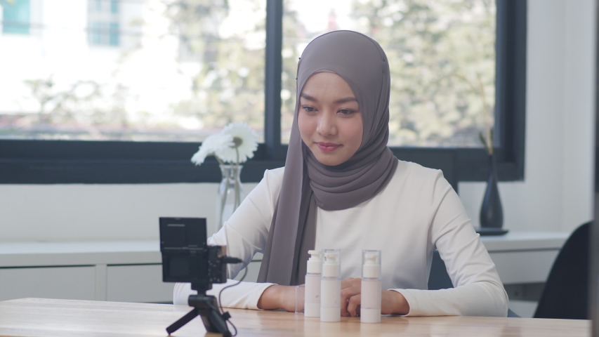 Beauty blogger present beauty cosmetics sitting in front camera for recording video. Beautiful young Asian muslim woman use cosmetics review make up tutorial broadcast live video to social network. Royalty-Free Stock Footage #1056199199