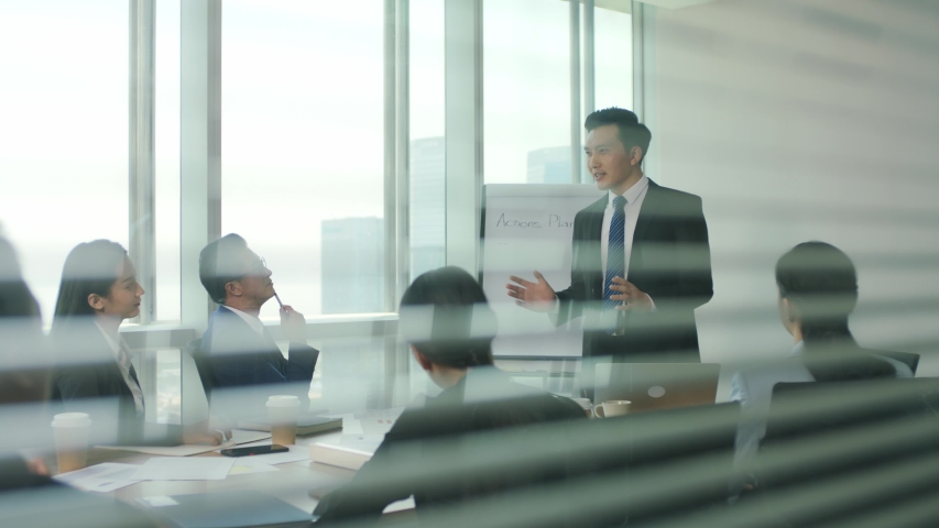 Through the glass and blinds shot of a team of asian business people men and women meeting in modern office conference room | Shutterstock HD Video #1056200063