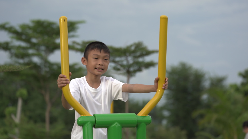 Kids playing and exercing on public outdoor gym park, boy children holding equipment and smile to enjoy play and exercise for good health for outside reaction on blurred background, Asian kids child