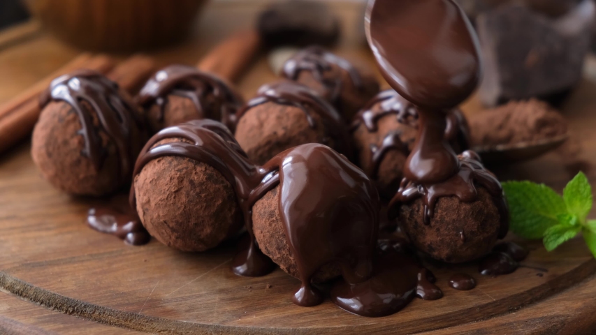 Glazed chocolate truffles on wooden background. Pouring chocolate glaze on chocolate truffles. Domestic confectionery | Shutterstock HD Video #1056200945
